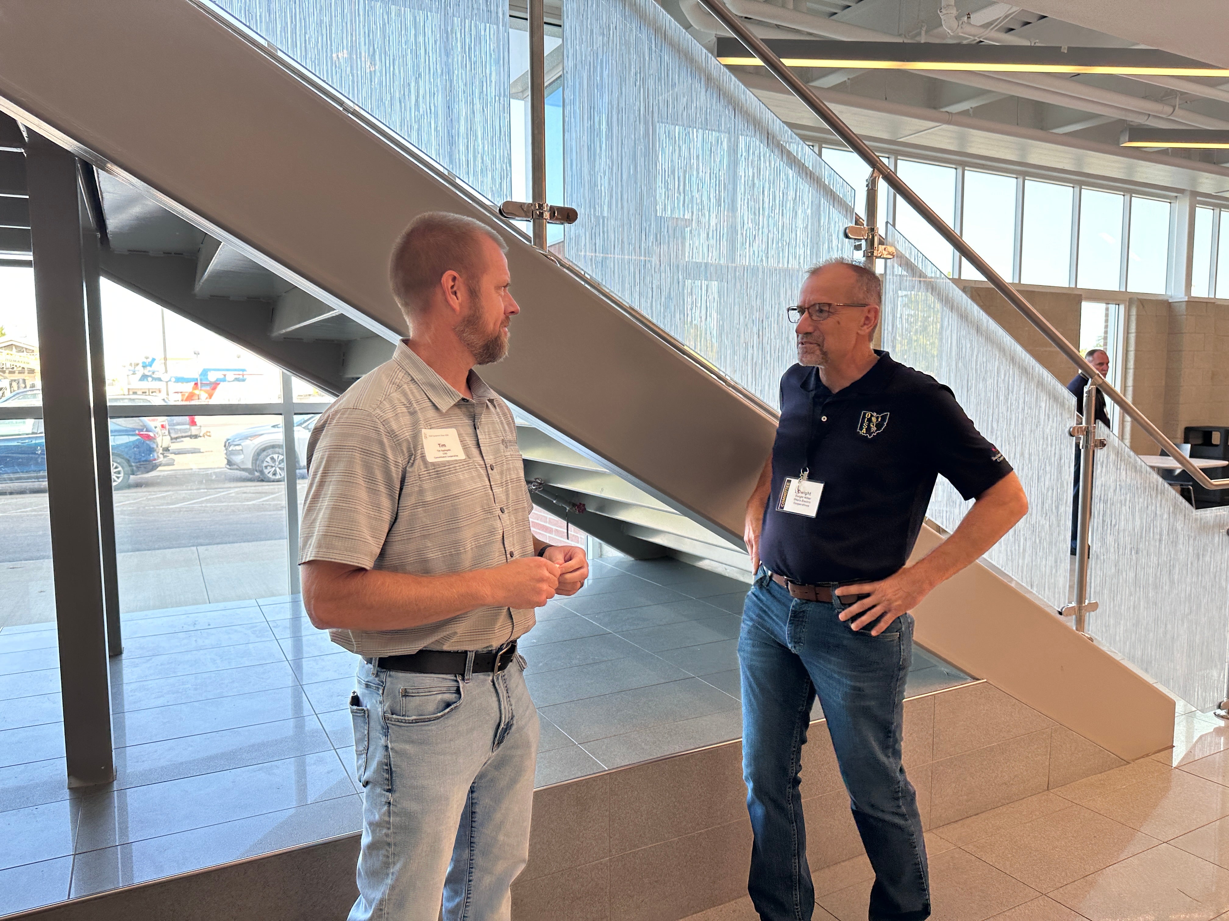 Two men talking in front of a set of stairs
